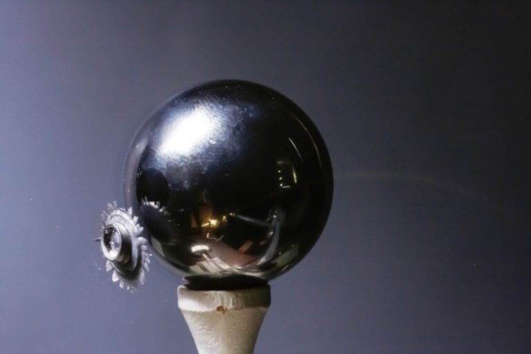 Air pellet rebounding from steel ball on golf tee. The arc in front of the ball is the trajectory of the specular highlight